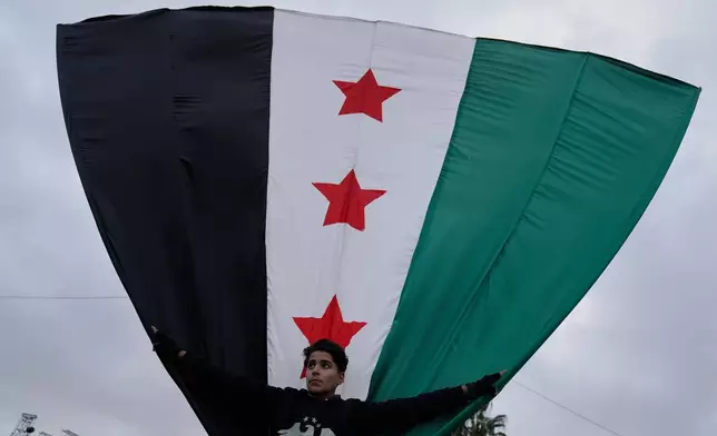 A Syrian man waves his country flag during celebrations marking the first anniversary of the ousting of former President Bashar Assad in Damascus, Syria, Monday, Dec. 8, 2025. (AP Photo/Hussein Malla)