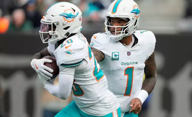 Miami Dolphins quarterback Tua Tagovailoa (1) hands off the ball to running back De'Von Achane (28) during the first quarter of an NFL football game, Sunday, Dec. 7, 2025, in East Rutherford, N.J. (AP Photo/Yuki Iwamura)