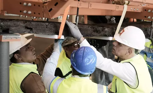 Archeologists carry an ancient wooden block as they reassemble the second solar boat of King Khufu, at the Grand Egyptian Museum in Giza, Egypt, Tuesday, Dec. 23, 2025. (AP Photo/Amr Nabil)