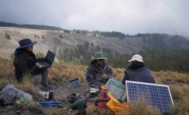 Karina Rodriguez, left, a master's student, and Marco Calo, center, a geophysicist at the National Autonomous University of Mexico (UNAM), collect information from a monitoring station on the slopes of the Popocatepetl volcano in Mexico, Friday, Dec. 5, 2025. (AP Photo/Eduardo Verdugo)