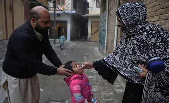 A health worker, right, administers a polio vaccine to a child at a neighbourhood in Peshawar, Pakistan, Monday, Monday, Dec. 15, 2025. (AP Photo/Muhammad Sajjad)