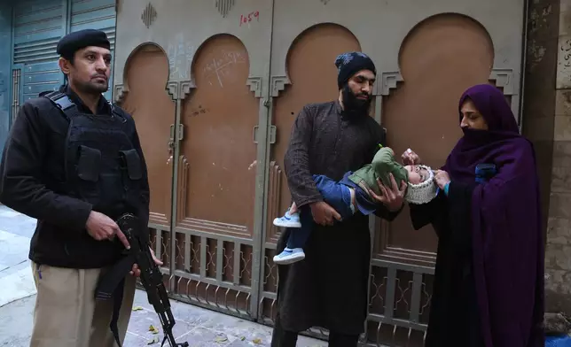 A police officer stands guard as a health worker, right, administers a polio vaccine to a child at a neighbourhood in Peshawar, Pakistan, Monday, Monday, Dec. 15, 2025. (AP Photo/Muhammad Sajjad)