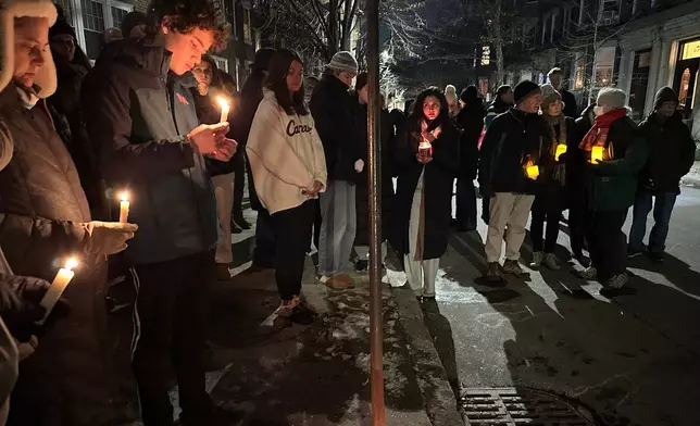A crowd of people holding candles gather outside the home of Massachusetts Institute of Technology professor Nuno F.G. Loureiro in Brookline, Mass., Tuesday, Dec. 16, 2025. (AP Photo/Leah Willingham)