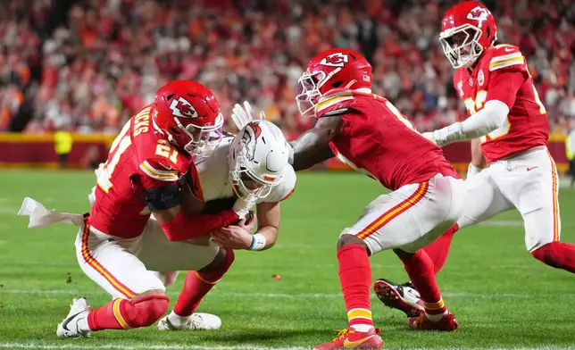 Denver Broncos quarterback Bo Nix, center, pushes through across the goal line to score on a run as Kansas City Chiefs safety Jaden Hicks (21), cornerback Kristian Fulton, second from right, and linebacker Drue Tranquill, right, try to stop him during the second half of an NFL football game Thursday, Dec. 25, 2025, in Kansas City. (AP Photo/Ed Zurga)