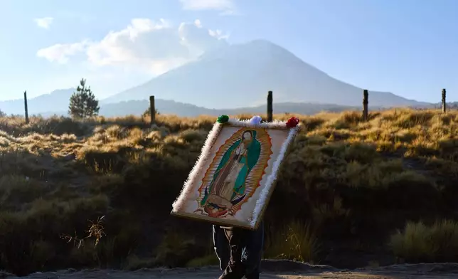 A pilgrim carries an image of the Virgin of Guadalupe past the Popocatepetl in Paso de Cortes on his way to Mexico City, Wednesday, Dec. 10, 2025. (AP Photo/Claudia Rosel)