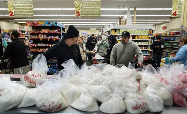 Alex Diaz, left, reaches for a bag of masa, a dough used to make tamales, as shoppers wait in line at Amapola Market in Downey, Calif., Tuesday, Dec. 23, 2025. (AP Photo/Jae C. Hong)