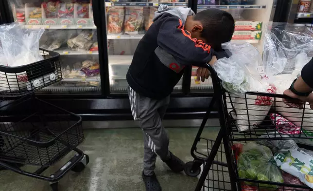 Antonio Alvarez, 11, rests his head on a shopping cart as he and his mother wait in line to buy masa, a dough used to make tamales, at Amapola Market in Downey, Calif., early Tuesday morning, Dec. 23, 2025. (AP Photo/Jae C. Hong)