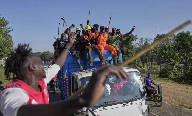 Spectators escort a truck where a bull is loaded, waving their chasing sticks and ululating, on the way to a bullfight in Kakamega, Kenya, Saturday, Nov. 29, 2025. (AP Photo/Brian Inganga)