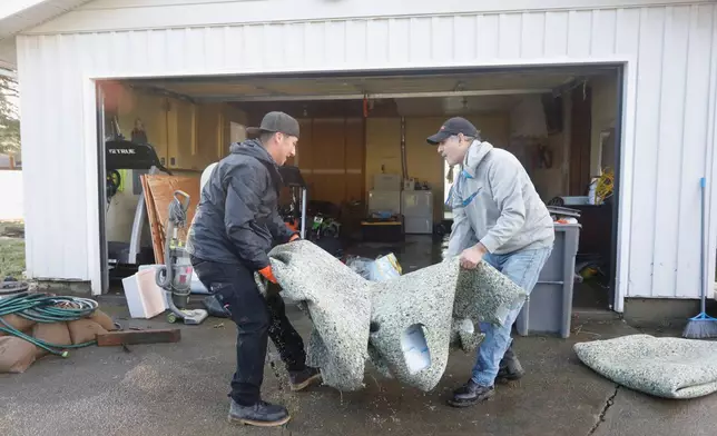 Men remove a wet carpet from a house damaged by floodwaters in Burlington, Washington, Saturday, Dec. 13, 2025. (AP Photo/Manuel Valdes)