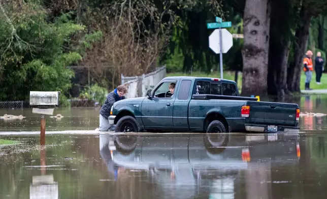A man pushes a truck through a neigbhorhood flooded by the Skagit River on Friday, Dec. 12, 2025, in Burlington. (AP Photo/Stephen Brashear)