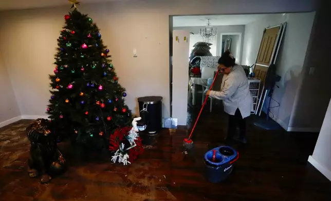 Fracis Tarango mops inside her daughters' home damaged by floodwaters in Burlington, Wash., Saturday, Dec. 13, 2025. (AP Photo/Manuel Valdes)