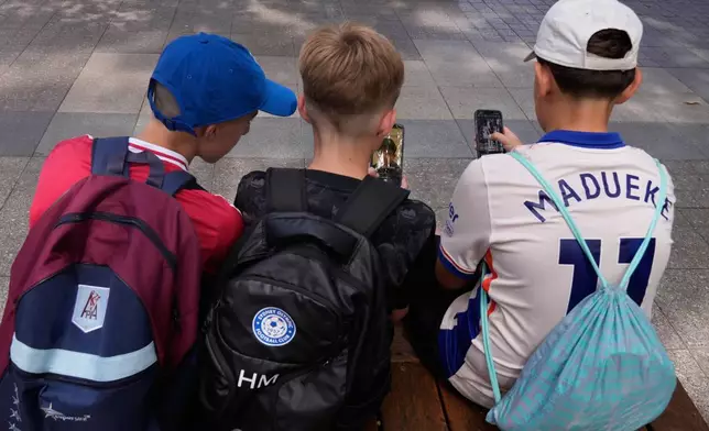 Hugo Winwood-Smith, right, Hardy Macpherson and Edan Abou, left, all 11-years-old, use their phones while sitting outside a school in Sydney, Monday, Dec. 8, 2025. (AP Photo/Rick Rycroft)