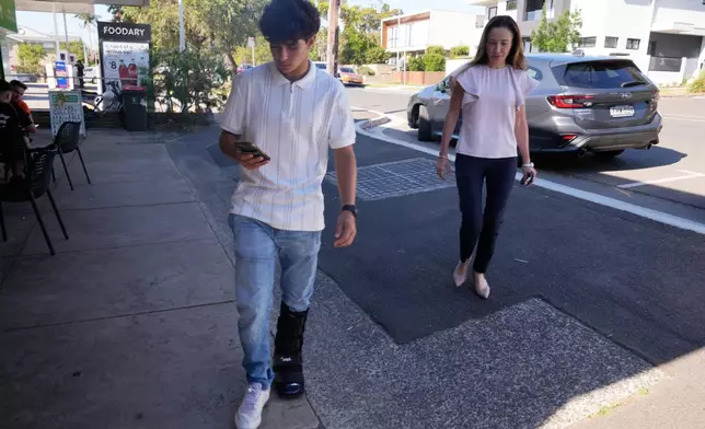 Noah Jones, left, uses his phone as his mother Renee, walks toward him in Sydney, Tuesday, Dec. 9, 2025. (AP Photo/Rick Rycroft)