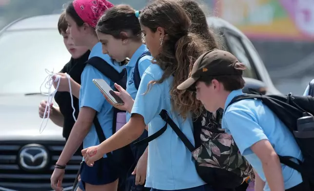 A school girl uses her phone as she walks with a group of kids in Sydney, Monday, Dec. 8, 2025. (AP Photo/Rick Rycroft)