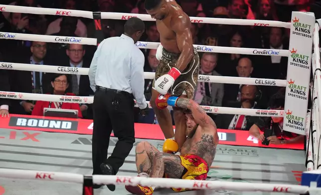 Jake Paul falls on the canvas after being hit by Anthony Joshua during their heavyweight boxing match, Friday, Dec. 19, 2025, in Miami, Fla. (AP Photo/Lynne Sladky)