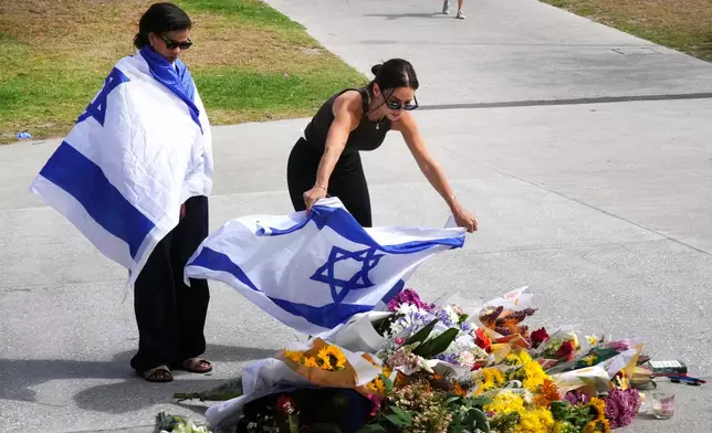 A woman places an Israeli flag over flowers outside Bondi Pavilion at Sydney's Bondi Beach, Monday, Dec. 15, 2025, a day after a shooting. (AP Photo/Mark Baker)