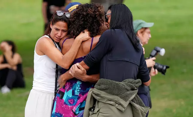 People offer hugs to each other at a flower memorial placed outside Bondi Pavilion at Sydney's Bondi Beach, Monday, Dec. 15, 2025, a day after a shooting. (AP Photo/Mark Baker)