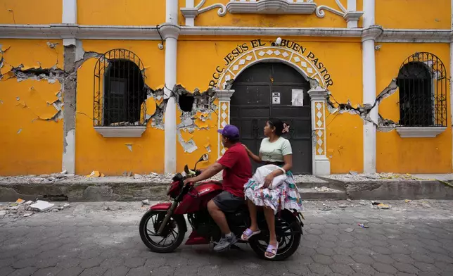 A couple ride past a community hall damaged by dozens of earthquakes and aftershocks recorded in a matter of hours in Santa Maria de Jesus, Guatemala, July 9, 2025. (AP Photo/Moises Castillo, File)