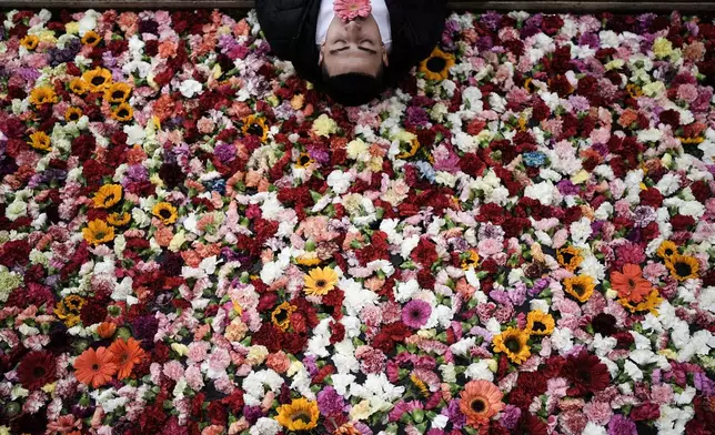A pedestrian poses for a photo on the edge of a water canal filled with flowers in downtown Bogota, Colombia, during the opening of the city's first art biennial, Sept. 20, 2025. (AP Photo/Ivan Valencia, File)