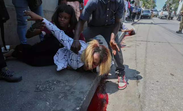 A woman cries after her friend, Valerie Saint-Fort, behind, fell dead from a bullet wound after soldiers fired their guns into the air as a tribute during the funeral of two soldiers in Port-au-Prince, Haiti, March 17, 2025. (AP Photo/Odelyn Joseph, File)
