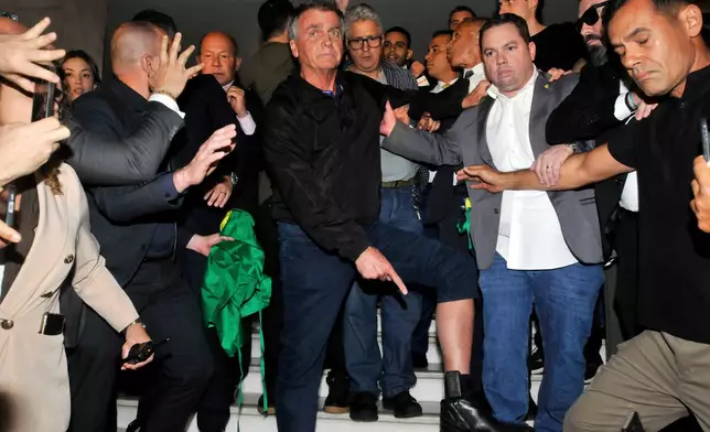 Brazil's former President Jair Bolsonaro points to his electronic ankle monitor that the Supreme Court ordered him to wear, at Congress in Brasilia, Brazil, July 21, 2025. (AP Photo/Minervino Junior, CB/D.A Press, File)