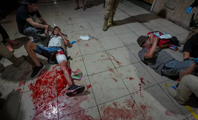 A man wounded in a fight smokes next to his injured friend as they wait for an ambulance after a fight in a shopping arcade in downtown Santiago, Chile, Dec. 2, 2025. (AP Photo/Esteban Felix, File), File)