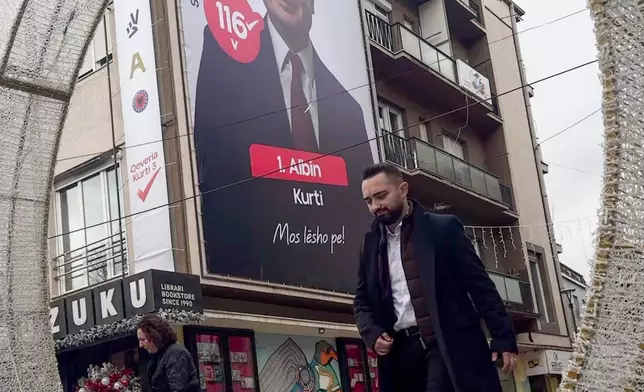 People walk past a giant banner of the leader of VV (Selfdetermination) political party Albin Kurti, in the capital Pristina on Wednesday, Dec. 24, 2025. (AP Photo/Visar Kryeziu)