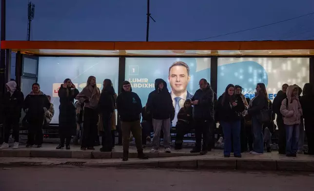 People waiting in the iluminated bus station with banners of LDK (Democratic League of Kosovo) leader Lumir Abdixhiku in capital Pristina on Thursday, Dec. 25, 2025. (AP Photo/Visar Kryeziu)