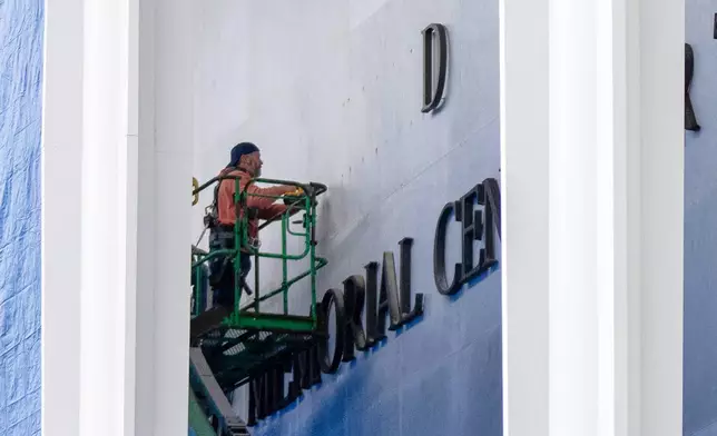 A worker drills holes near letters being installed above the signage on the Kennedy Center on Friday, Dec. 19, 2025, in Washington. (AP Photo/Mark Schiefelbein)