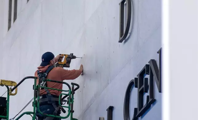A worker drills holes near letters being installed above the signage on the Kennedy Center on Friday, Dec. 19, 2025, in Washington. (AP Photo/Mark Schiefelbein)