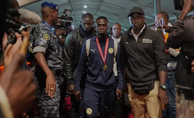 Senegal's Krépin Diatta, center, is accompanied by securitties as the team arrives following their victory in the Africa Cup of Nations soccer tournament, in Ndiass, Senegal, Tuesday, Jan. 20, 2026. (AP Photo/Misper Apawu)