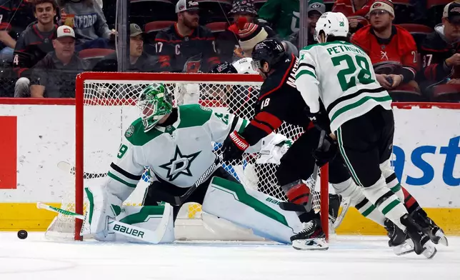 Carolina Hurricanes' Jordan Martinook, center, drives the puck between Dallas Stars' Mavrik Bourque (22) and goaltender Jake Oettinger during the first period of an NHL hockey game in Raleigh, N.C., Tuesday, Jan. 6, 2026. (AP Photo/Karl DeBlaker)