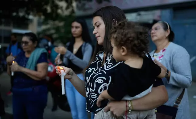 Juliana Flores holds her son and a candle while calling for her parents to be set free outside El Helicoide, the headquarters of Venezuela's intelligence service and detention center, in Caracas, Venezuela, Friday, Jan. 9, 2026 after the government announced prisoners would be released.(AP Photo/Ariana Cubillos)