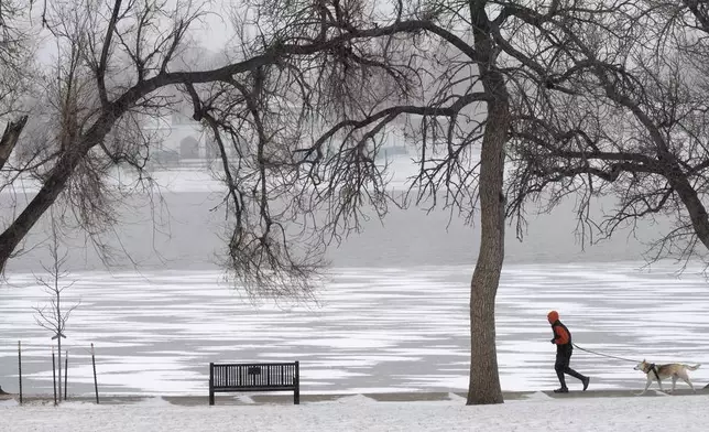 A runner and his dog circle a frozen Prospect Lake in Colorado Springs, Colo., Friday, Jan. 23, 2026, as snow and extremely cold weather hits the Pikes Peak Region. (Christian Murdock/The Gazette via AP)