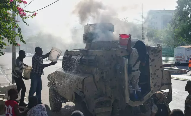 Police and civilians attempt to put out a fire set by gang members on an armored police vehicle in a gang-controlled area of Port-au-Prince, Haiti, Monday, Jan. 19, 2026. (AP Photo/Odelyn Joseph)
