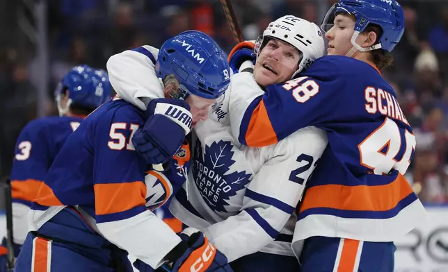New York Islanders' Emil Heineman and Matthew Schaefer (48) hold back Toronto Maple Leafs' Jake McCabe, center, during a fight in the first period of an NHL hockey game, Saturday, Jan. 3, 2026, in New York. (AP Photo/Heather Khalifa)