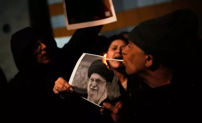 A demonstrator lights a cigarette with a burning poster depicting Supreme Leader Ayatollah Ali Khamenei during a rally in support of Iran's anti-government protests, in Holon, Israel Wednesday, Jan. 14, 2026. (AP Photo/Ohad Zwigenberg)