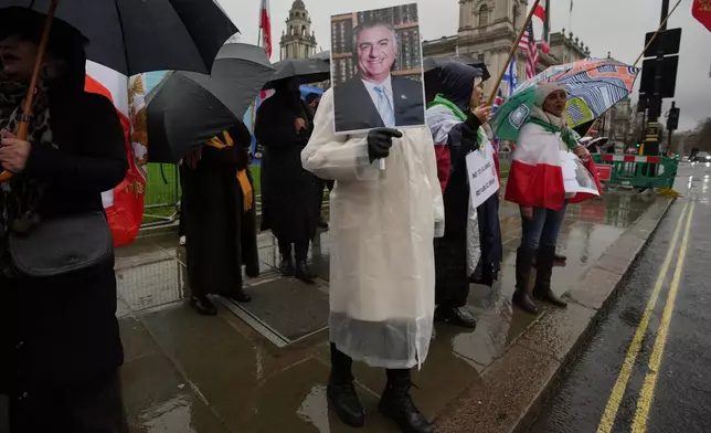 Protesters hold up placards showing Iran’s exiled crown prince Reza Pahlavi as they demonstrate outside the House of Parliament, in London, England, Tuesday, Jan. 13, 2026. (AP Photo/Kin Cheung)