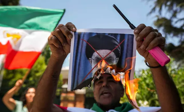 A demonstrator burns a poster of Iran's Supreme Leader Ayatollah Ali Khamenei during a rally in support of anti-government protests in Iran, outside Iran's embassy in Santiago, Chile, Tuesday, Jan. 13, 2026. (AP Photo/Esteban Felix)