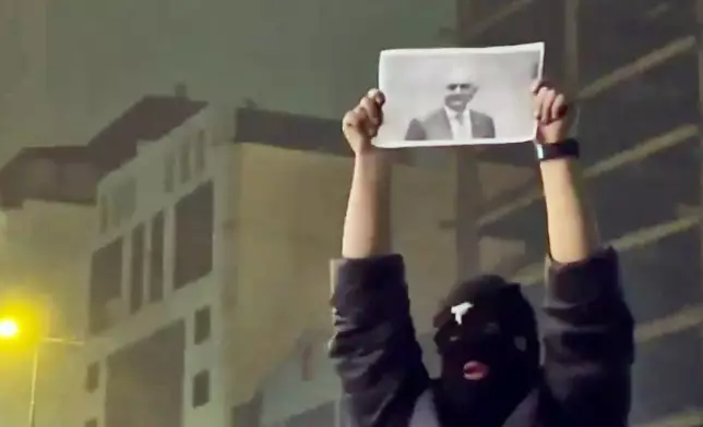 In this frame grab from video obtained by the AP outside Iran, a masked demonstrator holds a picture of Iran's Crown Prince Reza Pahlavi during a protest in Tehran, Iran, Friday, January. 9, 2026. (UGC via AP)