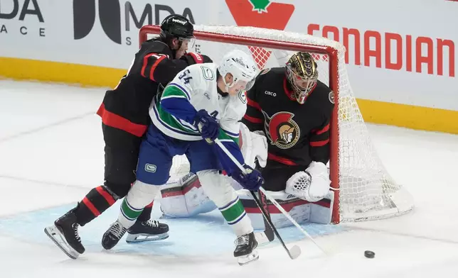 Vancouver Canucks center, Aatu Raty (54) tries to tip the puck past Ottawa Senators goaltender Leevi Merilainen (1) as he is pressured by defenseman Jordan Spence (10) during first period NHL action in Ottawa, Tuesday, Jan. 13, 2026. (Adrian Wyld/The Canadian Press via AP)