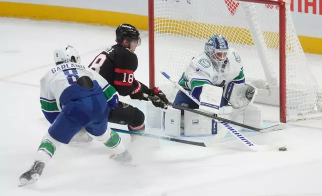 Vancouver Canucks goaltender Kevin Lankinen (32) poke checks the puck away from Ottawa Senators center Tim Stutzle (18) as he is pressured by Canucks right wing Conor Garland (8) during second period NHL action in Ottawa, Tuesday, Jan. 13, 2026. (Adrian Wyld/The Canadian Press via AP)