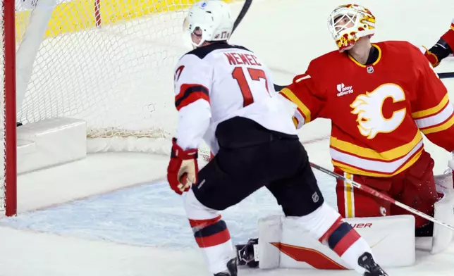 New Jersey Devils' Simon Nemec, left, scores in overtime against Calgary Flames goalie Devin Cooley during NHL hockey game action in Calgary, Alberta, Monday, Jan. 19, 2026. (Larry MacDougal/The Canadian Press via AP)