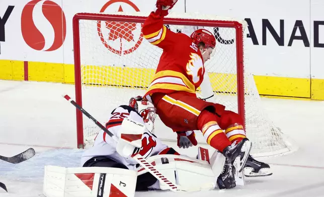 After a shot by Calgary Flames' Nazem Kadri (not shown) scores against New Jersey Devils goalie Jacob Markstrom, left, as Calgary Flames' Connor Zary, right, falls into the net during second-period NHL hockey game action in Calgary, Alberta, Monday, Jan. 19, 2026. (Larry MacDougal/The Canadian Press via AP)