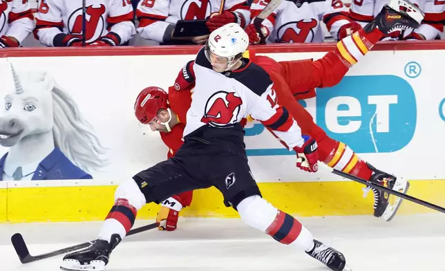 New Jersey Devils' Cody Glass (12) collides with Calgary Flames' Nazem Kadri, back, during first-period NHL hockey game action in Calgary, Alberta, Monday, Jan. 19, 2026. (Larry MacDougal/The Canadian Press via AP)