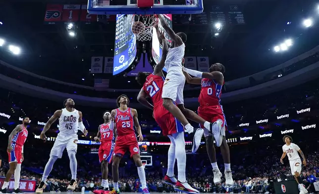 Cleveland Cavaliers' Evan Mobley, center, dunks between Philadelphia 76ers' Tyrese Maxey, right, and Joel Embiid during the first half of an NBA basketball game Friday, Jan. 16, 2026, in Philadelphia. (AP Photo/Matt Slocum)