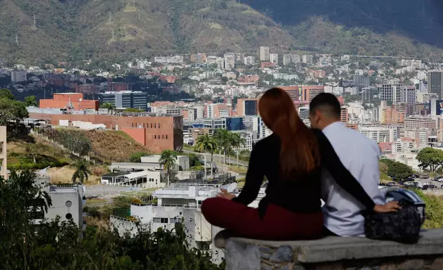 A couple sits on a bench at a viewpoint overlooking the U.S. embassy, center left, in Caracas, Venezuela, Friday, Jan. 9, 2026. (AP Photo/Cristian Hernandez)