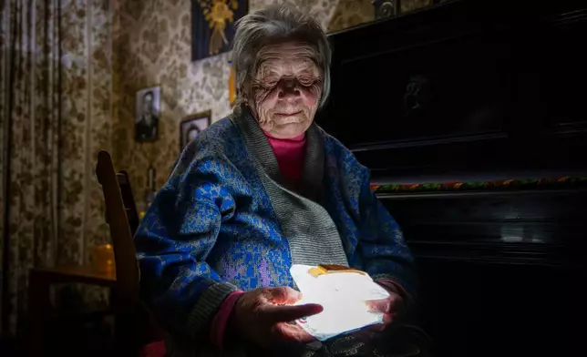 Raisa Derhachova holds a homemade flashlight during a power outage caused by regular Russian air strikes on the country's energy facilities in Kyiv, Ukraine, Tuesday, Jan. 13, 2026. (AP Photo/Dan Bashakov)