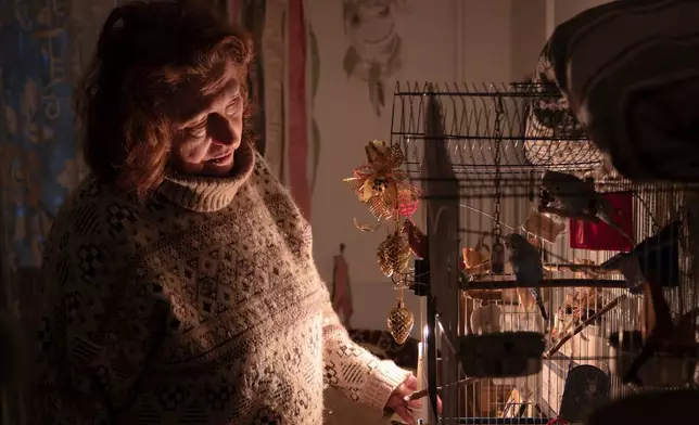 Tetyana Tatarenkova stands with a candle near a cage with ploughs during a power outage caused by regular Russian air strikes on the country's energy facilities in Kyiv, Ukraine, Tuesday, Jan. 13, 2026. (AP Photo/Dan Bashakov)