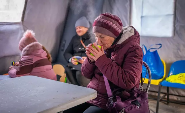 A woman gets warm with a hot cup of tea at an emergency center set up to support people during power outages caused by Russia's regular air attacks on the country's energy objects in Boryspil, Ukraine, Wednesday, Jan. 14, 2026. (AP Photo/Dan Bashakov)